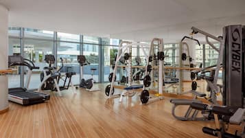 A modern gym with cardio machines, weightlifting equipment, and large windows offering views of the city.