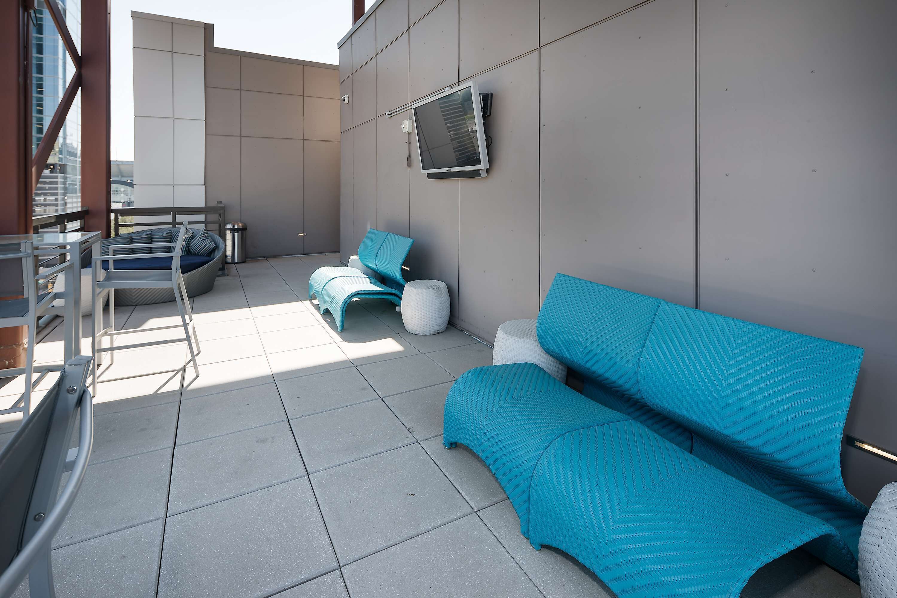 Un espace extérieur moderne aménagé avec un canapé et des fauteuils, un téléviseur à écran plat fixé au mur et une rambarde en métal.