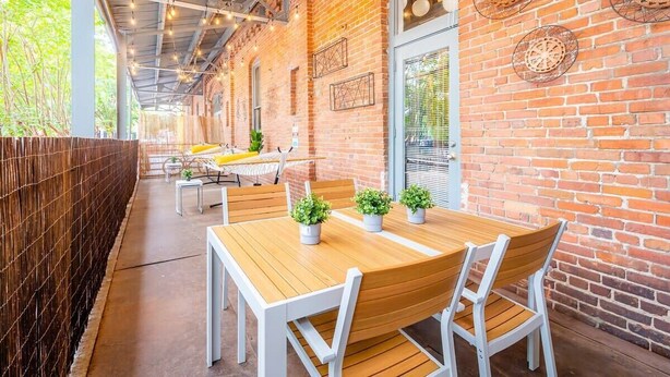 An outdoor dining area with brick walls, wooden tables, and potted plants. - 100 Year-Old Historic Brick 2BR Loft -Large Patio1 (Durham)
