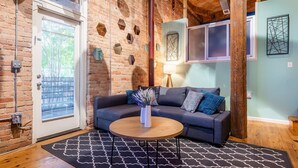A cozy living room with a brick wall, a gray sofa, a wooden coffee table, and a patterned rug. - 100 Year-Old Historic Brick 2BR Loft -Large Patio1 (Durham)