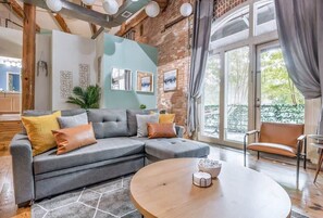 Uma sala de estar moderna com um sofá modular cinza, uma mesa de centro redonda de madeira e uma janela grande com cortinas.