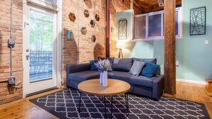 Ein gemütliches Zimmer mit Backsteinwand, grauem Sofa, Holztisch und einem gemusterten Teppich.