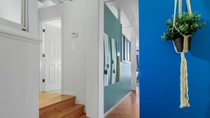 Un couloir avec un escalier en bois, une porte blanche et un mur bleu orné d’une plante en macramé.