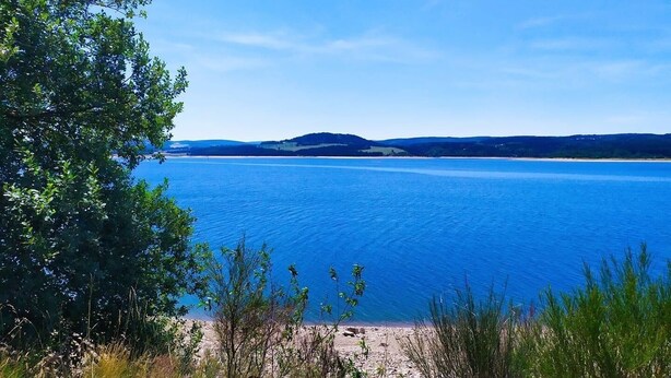A clear view of a lake with a sandy beach and surrounding greenery. - L'oustal du Lac, à Proximité du lac de Naussac et des Sentiers de Randonnée (Auroux)