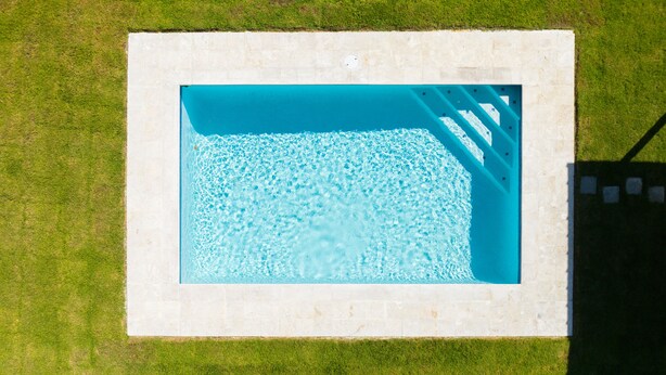 Vista aérea de una piscina rectangular con bordeado de azulejos, rodeada de césped.