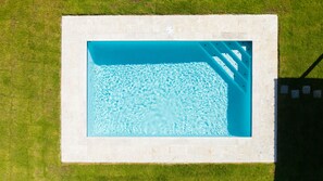 Vista aèria d'una piscina rectangular amb un videt de rajoles, envoltada per una zona verda.
