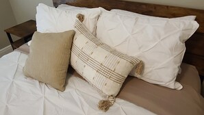 Un lit avec une literie blanche et deux coussins décoratifs, l’un beige et l’autre à motifs écossais.