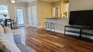 Un salon avec un plancher en bois, un canapé, un téléviseur et, au fond, un coin cuisine.