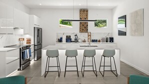 Una cocina moderna con armarios blancos, una isla central con taburetes de bar, horno empotrado y refrigerador de acero inoxidable.
