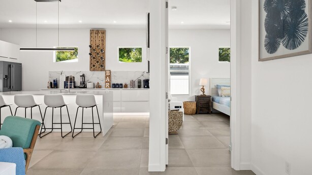 Una cocina moderna con taburetes de bar, un comedor con mesa y sillas, y un dormitorio con cama y mesita de noche.