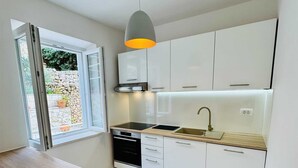 A modern kitchen with white cabinets, a wooden countertop, a built-in oven, and a pendant light. - KABLAR'S SUNNY SUITES 2BR apartment with balcony (Dubrovnik)