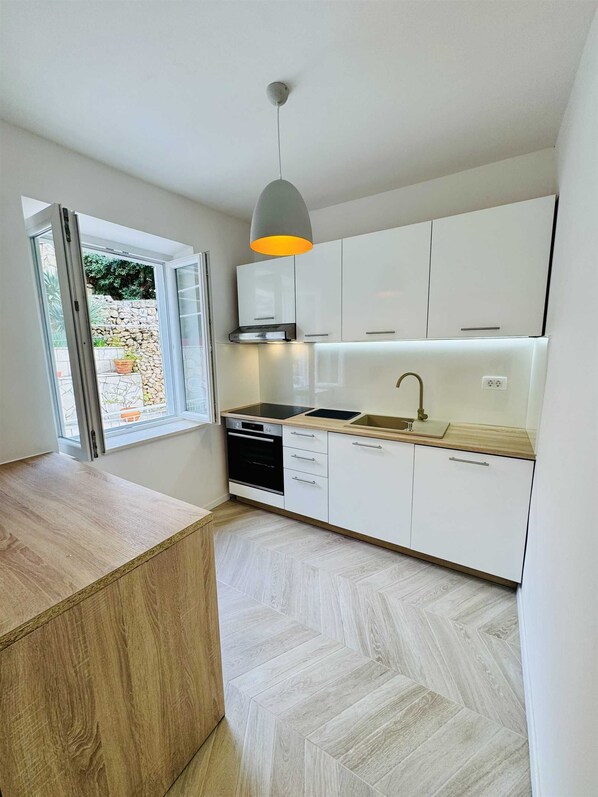 Una cocina moderna con armarios blancos, encimera de madera, horno empotrado y una lámpara colgante.