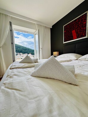 Habitación de hotel con cama, ropa de cama blanca, vista a la playa y un cuadro abstracto rojo en la pared.