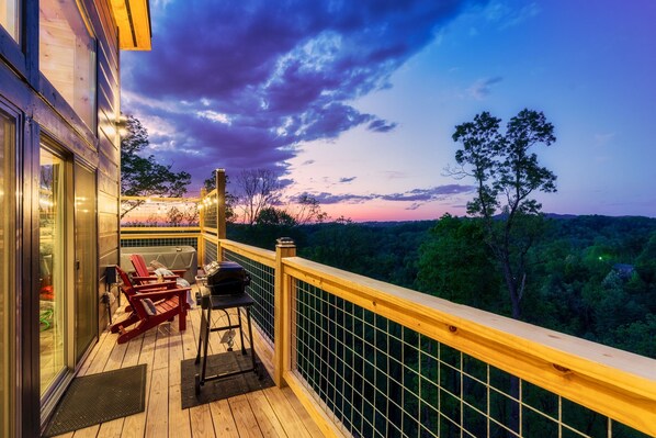 Une terrasse en bois avec un barbecue et des chaises rouges, donnant sur un paysage boisé.
