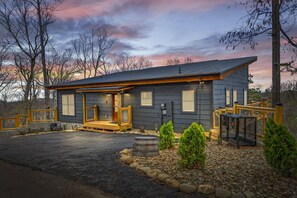 Une cabane en rondins à deux étages, à l’extérieur sombre, dotée d’une terrasse en bois et d’un chemin de pierre menant à l’entrée.