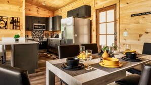 A modern kitchen with dark cabinets, a stainless steel refrigerator, and a microwave. There is a dining area with a table set for two, featuring black and yellow plates and glasses.