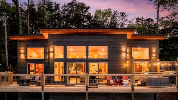 A modern two-story house with large windows, a balcony, and a wooden deck.
