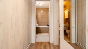 Un couloir étroit, doté d’un plancher et de murs en bois, mène à une salle de bain comprenant des toilettes, un lavabo et un espace douche.
