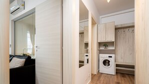Un espace de vie compact comprenant un canapé, un lave-linge et une armoire avec des portes miroir.