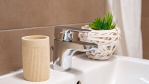 Un lavabo de salle de bain avec un robinet chromé, une tasse beige et un pot de fleurs en fibres tressées.