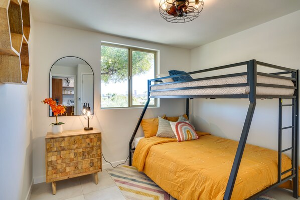 A bunk bed with a yellow bedspread, a dresser with a mirror, and a window with a view of trees.