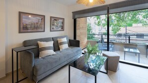 A modern living room with a grey sofa, black coffee table, and a hanging light fixture. There are two framed pictures on the wall and a large window with a view of the outside. - Departamento Nuevo en la Mejor Zona de la Ciudad (Mendoza)