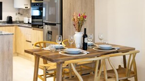 A wooden dining table set with plates, glasses, and a bottle of wine, with a vase of flowers in the center. - Departamento Nuevo en la Mejor Zona de la Ciudad (Mendoza)