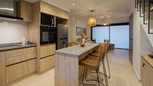 A modern kitchen with wooden cabinets, a central island, bar stools, and pendant lighting. - Departamento Nuevo en la Mejor Zona de la Ciudad (Mendoza)