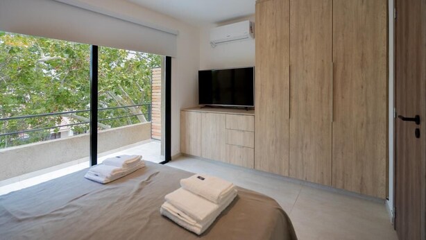 A modern bedroom with a large bed, a TV, and a wardrobe. - Departamento Nuevo en la Mejor Zona de la Ciudad (Mendoza)