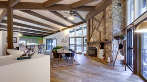 A spacious living area with a stone fireplace, wooden beams, and large windows.