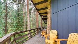 A wooden deck with Adirondack chairs overlooking a forest.