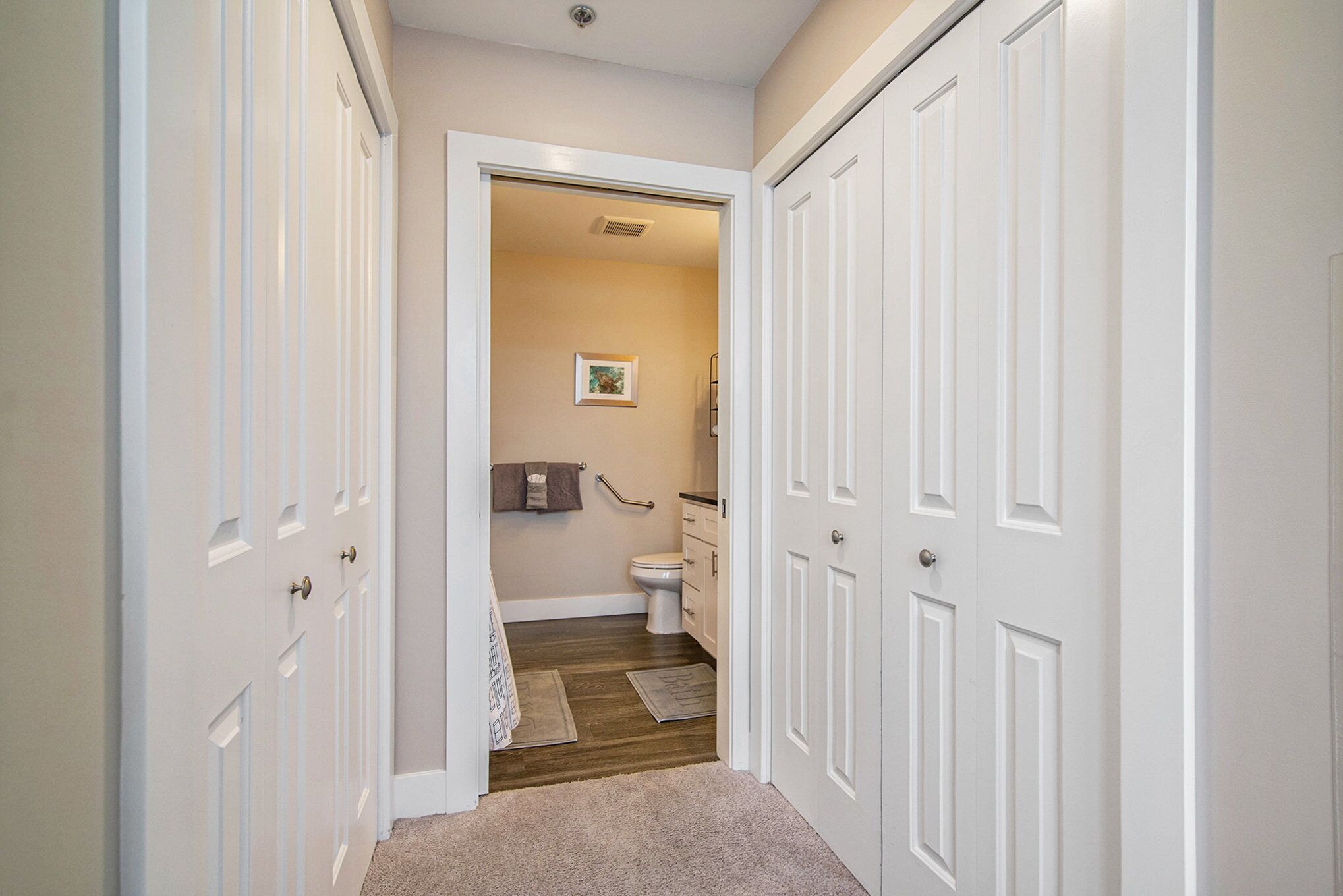 Un couloir étroit avec des portes blanches donnant sur une salle de bain.
