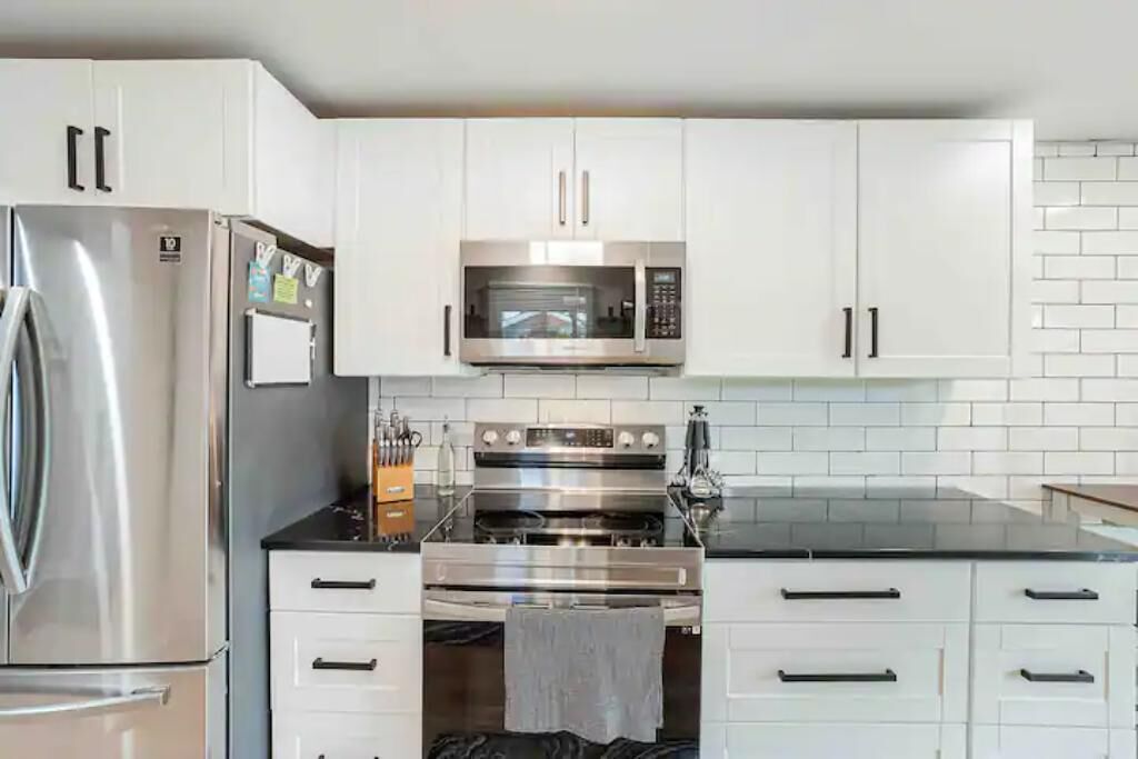 Een moderne keuken met witte kasten, roestvrijstalen apparatuur en een zwart aanrecht.