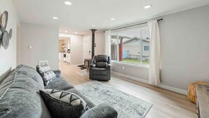 Un salon moderne avec un canapé gris, un fauteuil noir et une grande fenêtre agrémentée de rideaux.