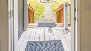 Une porte-fenêtre donnant sur un espace extérieur comprenant une terrasse en bois, un chemin de pierre et une clôture en bois.