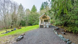 Een klein huisje met een veranda, omringd door een dicht bos.