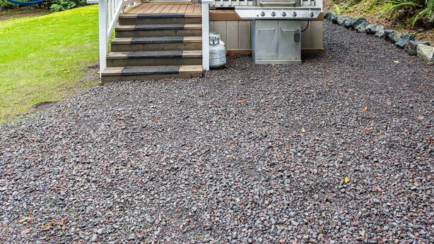 Een klein, gelijkvloers huisje met een veranda, een barbecue en een gasfles.