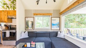 Een moderne woonkamer met een donkergrijze modulaire bank, een glazen salontafel en uitzicht op een bos door grote ramen.