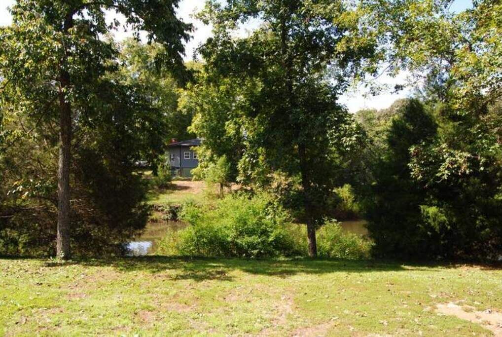 A house surrounded by dense trees and a small stream.