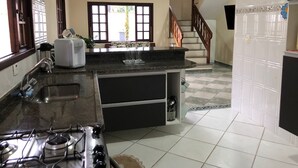 A kitchen with a gas stove, a sink, and a countertop. There is a staircase leading to another level. - Casa de Praia com Piscina Aquecida, ar Condicionado, Cervejeira e Bilhar!!! (Vista Linda Bertioga)