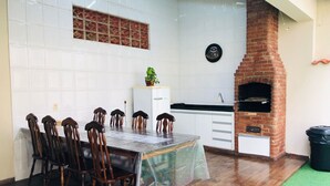 A dining area with a brick oven, white tiled walls, and a green rug. - Casa de Praia com Piscina Aquecida, ar Condicionado, Cervejeira e Bilhar!!! (Vista Linda Bertioga)