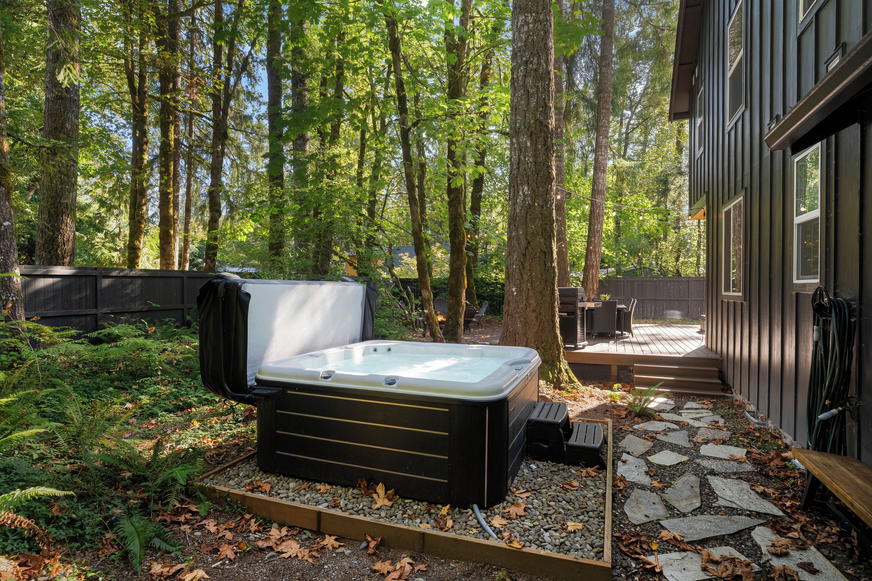 A hot tub in a forested backyard with a deck and outdoor furniture.