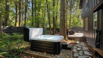 A hot tub in a forested backyard with a deck and outdoor furniture.