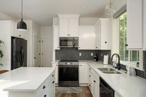 Cocina moderna con muebles blancos, un refrigerador negro, microondas, horno y pileta.