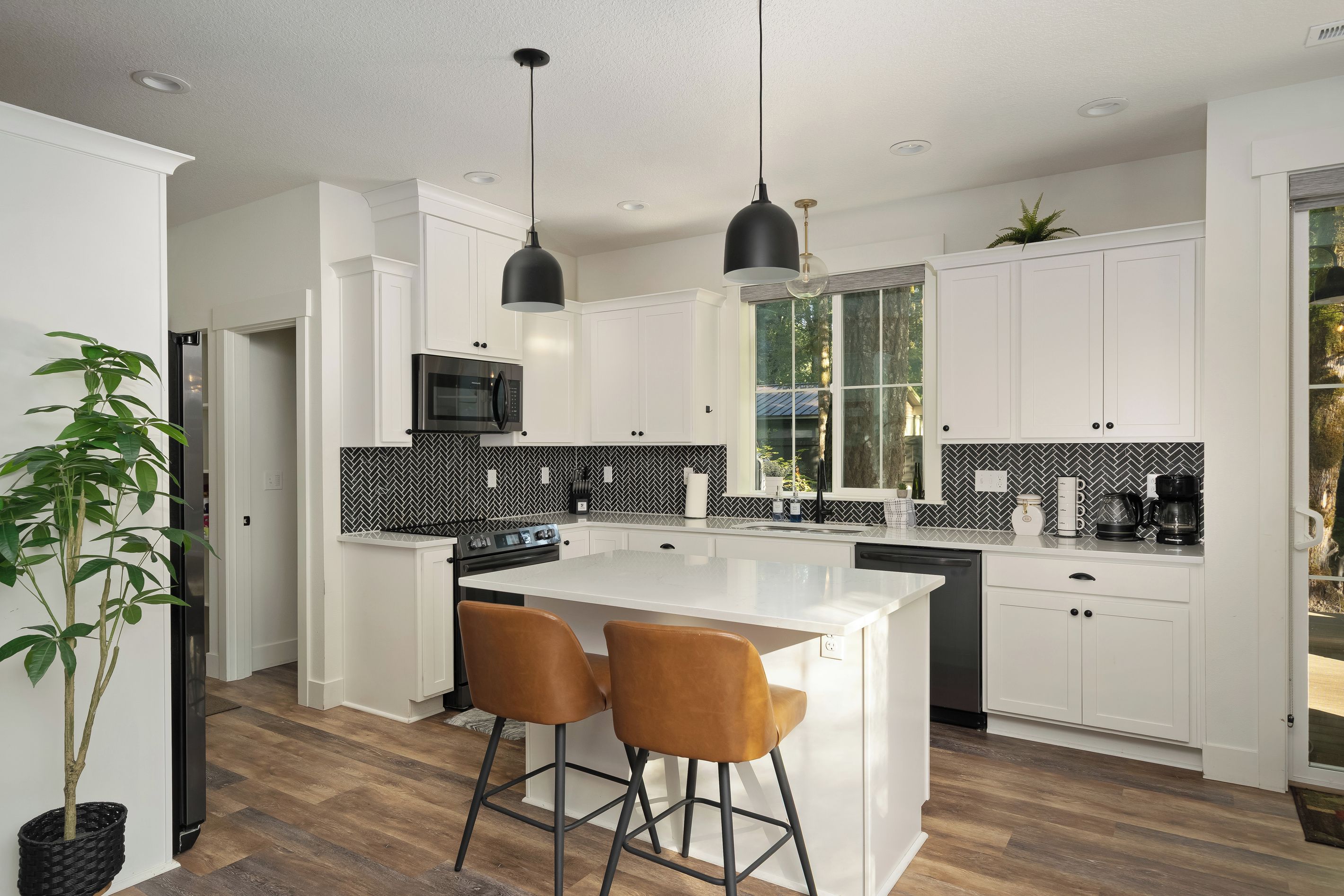 A modern kitchen with white cabinets, a black and white backsplash, a central island with two stools, and pendant lighting.