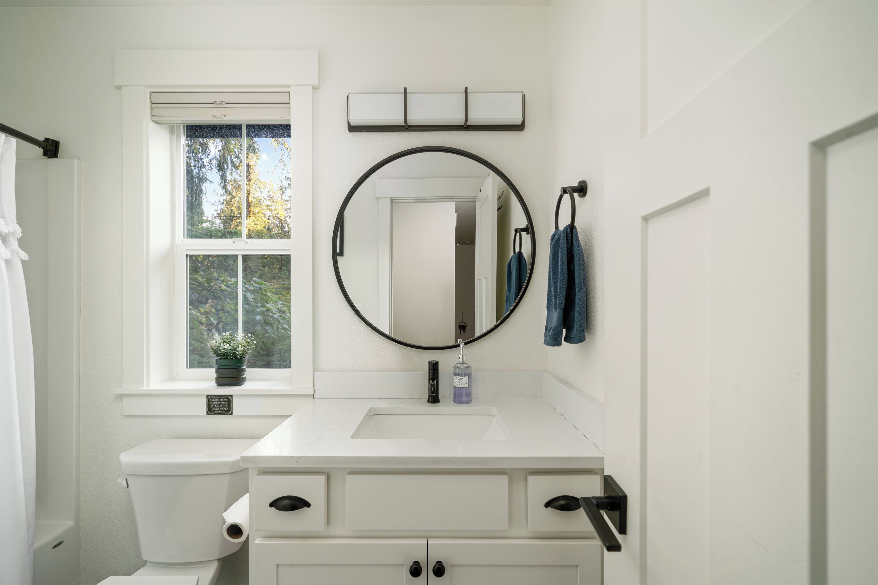A bathroom with a toilet, sink, mirror, and window.