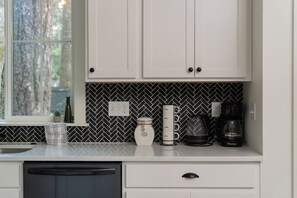 Una cocina con gabinetes blancos, un protector contra salpicaduras blanco y negro tipo espiga, una cafetera y un tostador.