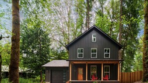 A two-story house with a dark exterior, a front porch with red chairs, and a garage.