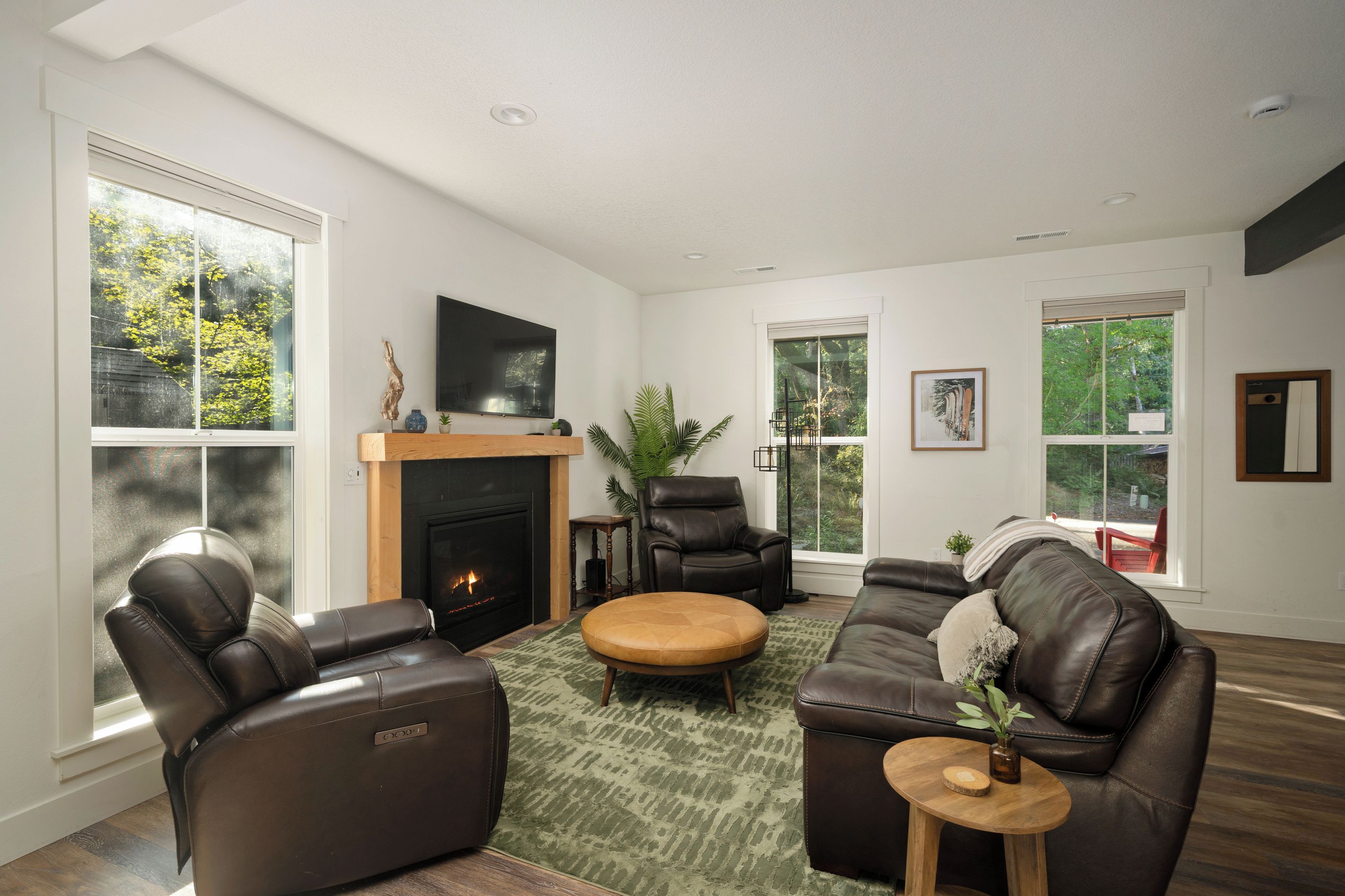 Ein modernes Wohnzimmer mit Ledersofas, einem Kamin und großen Fenstern mit Blick auf Grünflächen.