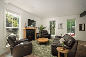 Ein modernes Wohnzimmer mit Ledersofas, einem Kamin und großen Fenstern mit Blick auf Grünflächen.